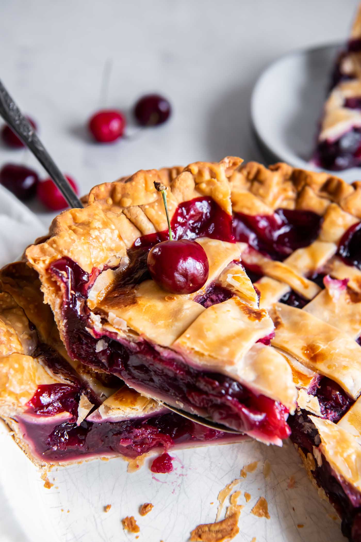 Slice of cherry pie on a pie server held over the pie.