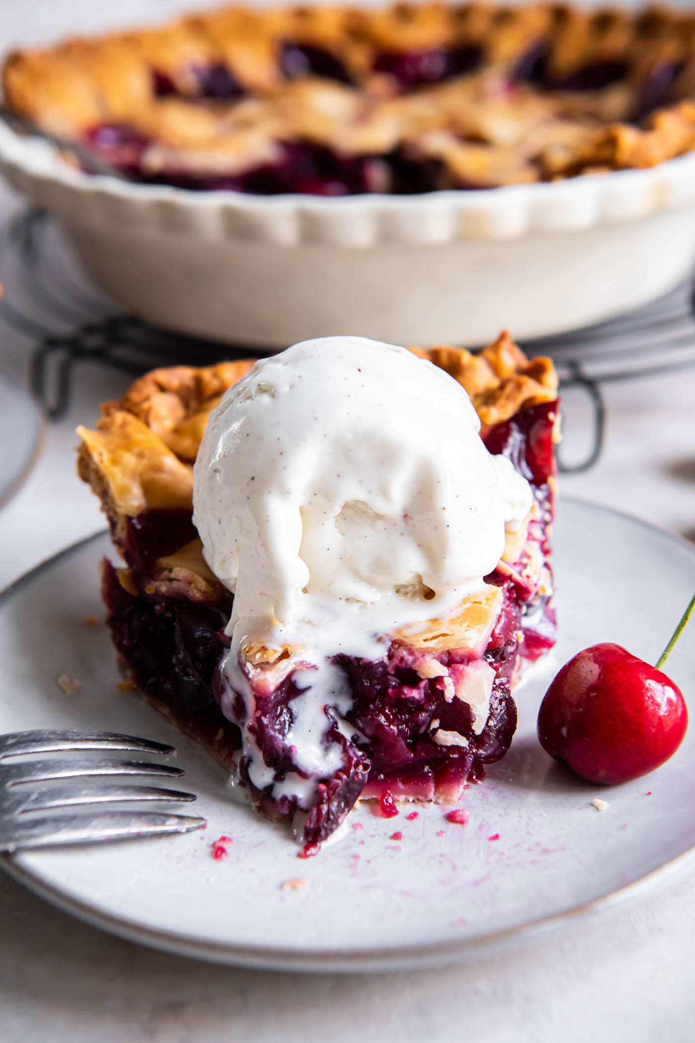Slice of cherry pie with a bite missing and a scoop of melty ice cream on top.
